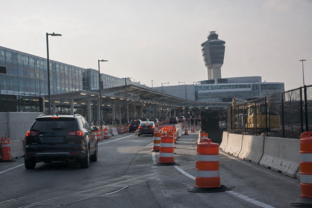 Traffic cones and construction barriers along an airport roadway with a terminal in the background