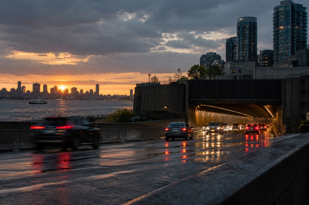 A highway tunnel entrance with headlights and brake lights streaking toward it at dusk