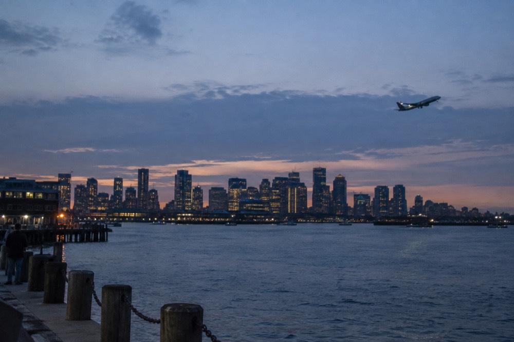 An airplane taking off over Boston Harbor with the downtown skyline in the distance
