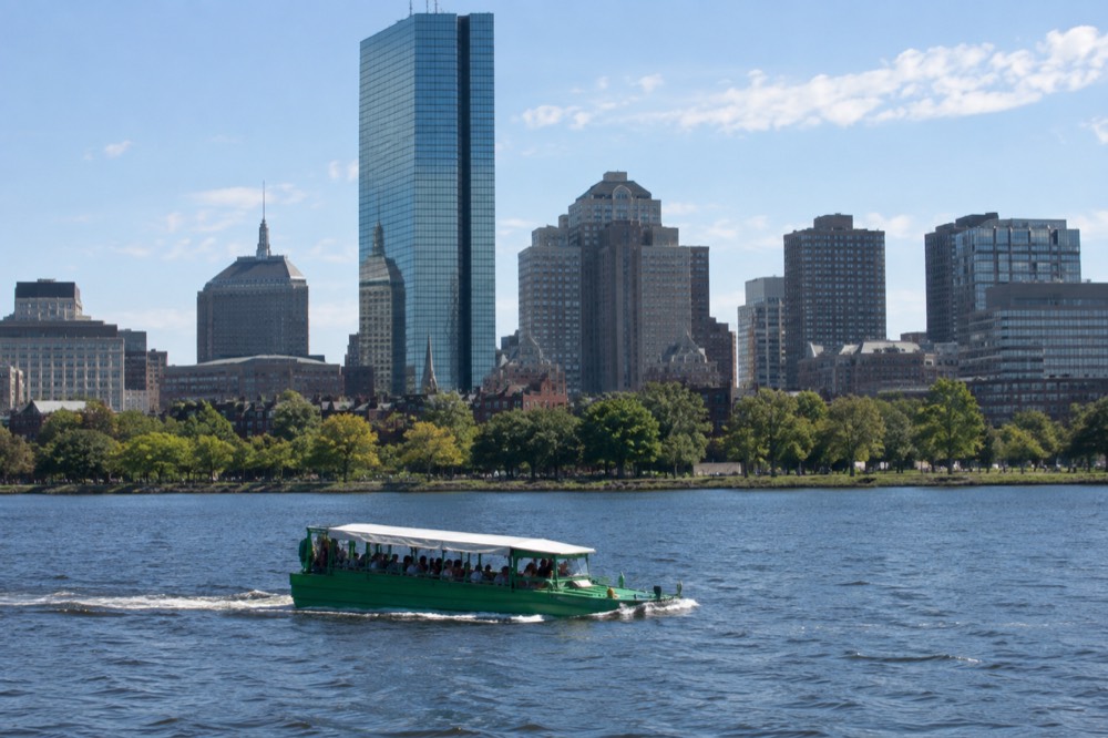A duck boat cruising on the Charles River with the Boston skyline behind it
