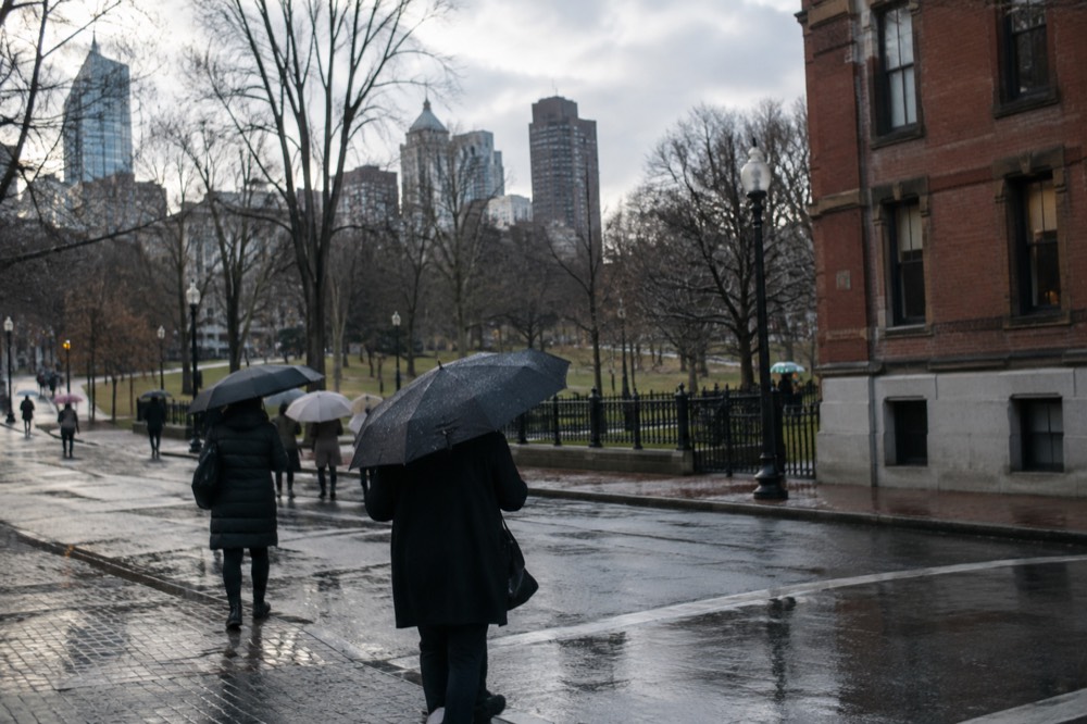 People with umbrellas crossing a rainy street near Boston brick buildings