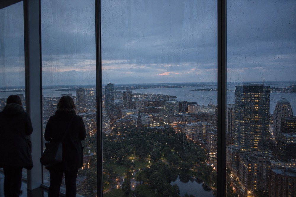 Rain streaking the glass walls of a high observation deck overlooking a city skyline