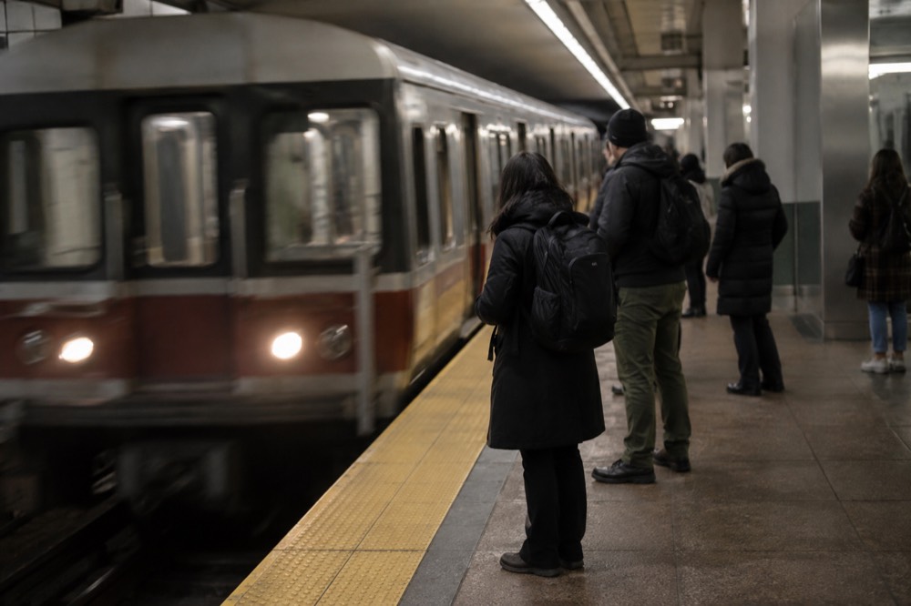 A subway platform with a train arriving and passengers waiting indoors