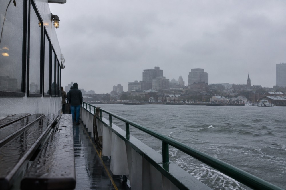 A ferry moving across gray water toward a coastal town in the rain