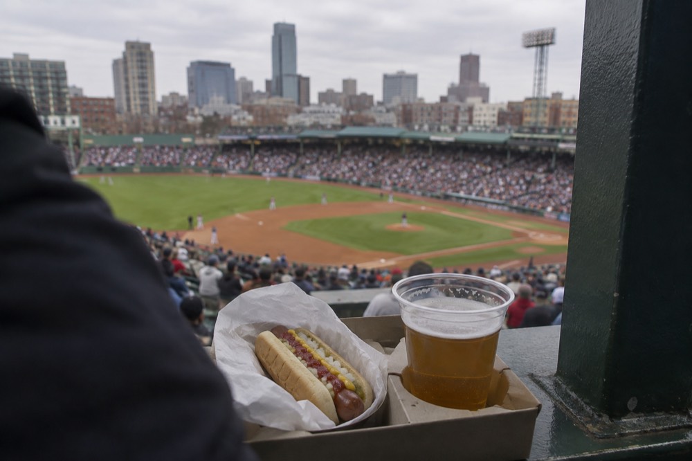 A hot dog and beer on a Fenway Park concession tray above the field