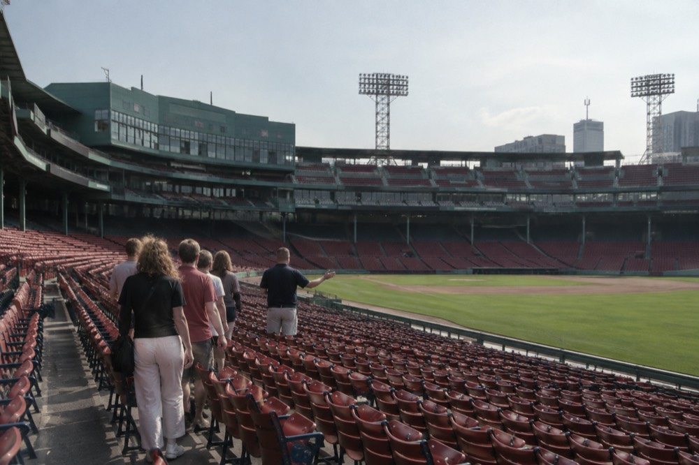 A guide leading a small group of visitors through the empty seats at Fenway Park