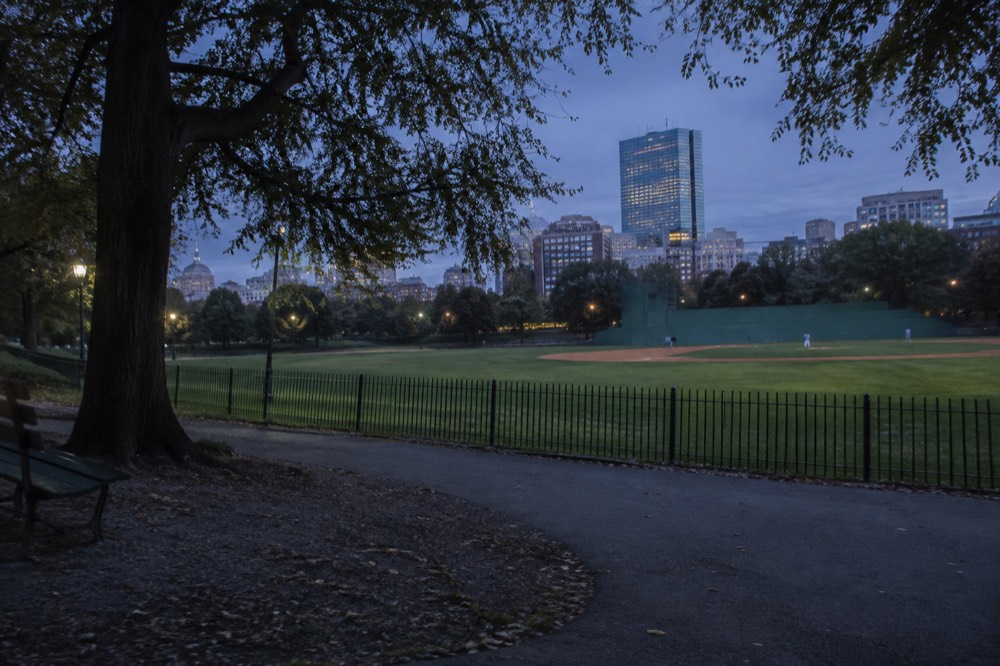 A green baseball field with a historic ballpark wall in the background