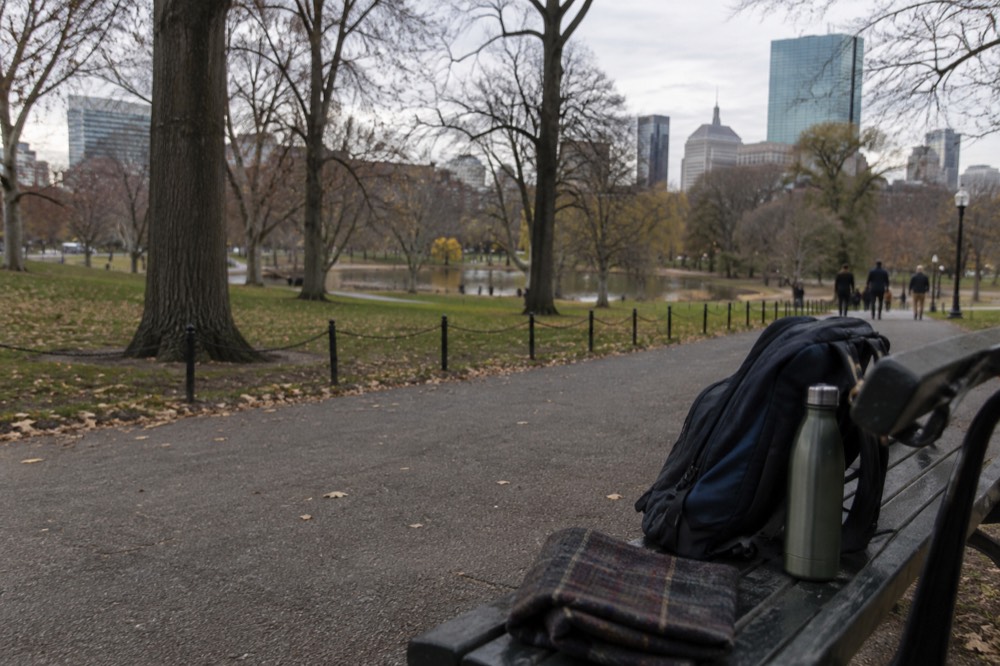 A small daypack on a bench with a water bottle, a folded map and sunglasses
