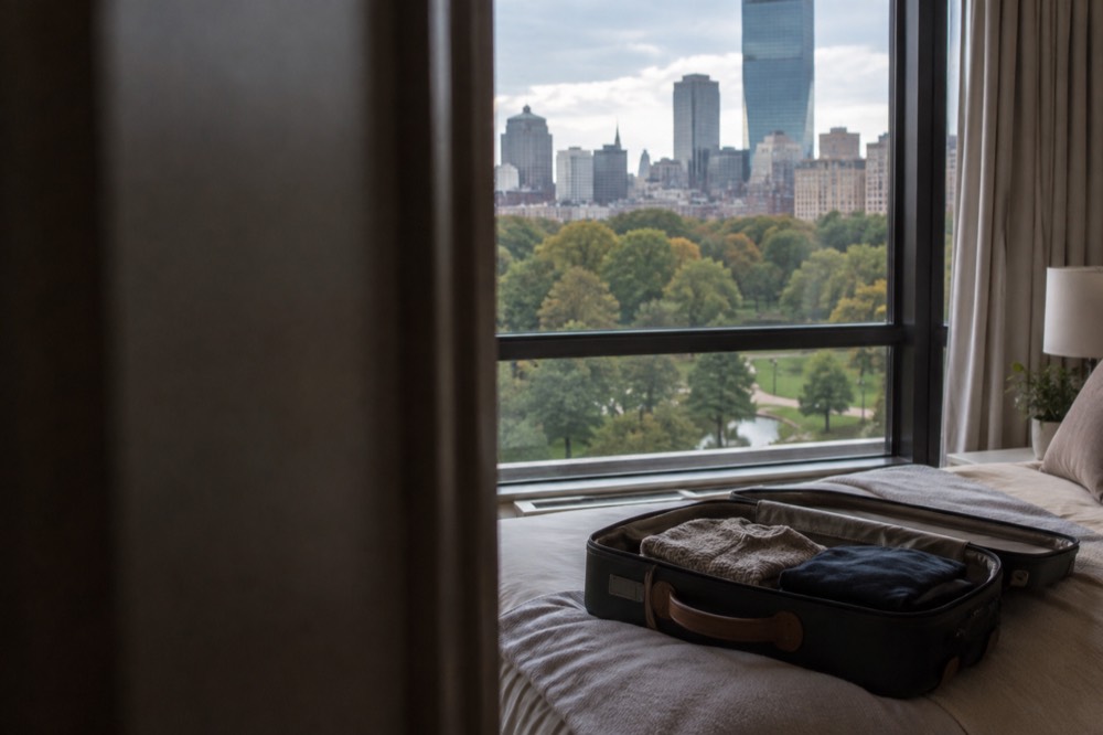 An open empty suitcase on a bed with a window showing a city skyline
