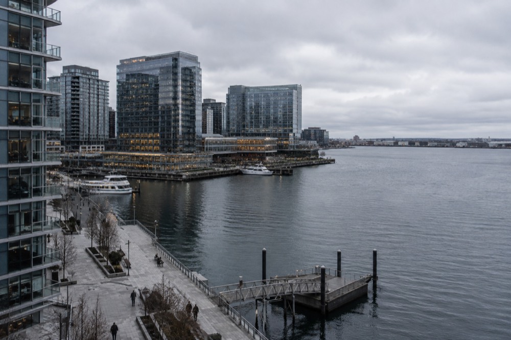 Modern glass hotel towers along the Boston Seaport waterfront with a harbor in the foreground