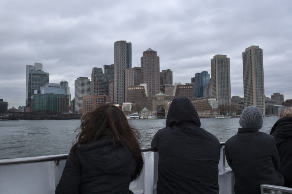 Visitors on a harbor cruise with the Boston skyline behind the boat