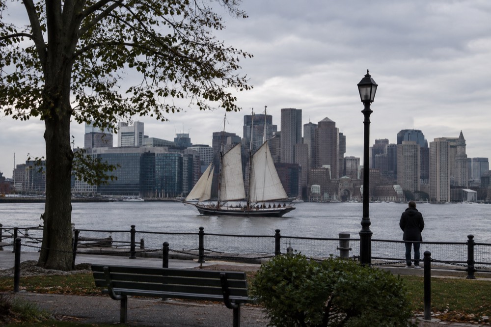 A wooden tall ship sailing on Boston Harbor with the city behind it