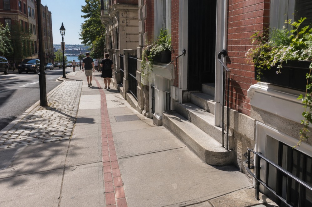 Red brick Freedom Trail line running along a Boston sidewalk with historic buildings behind it