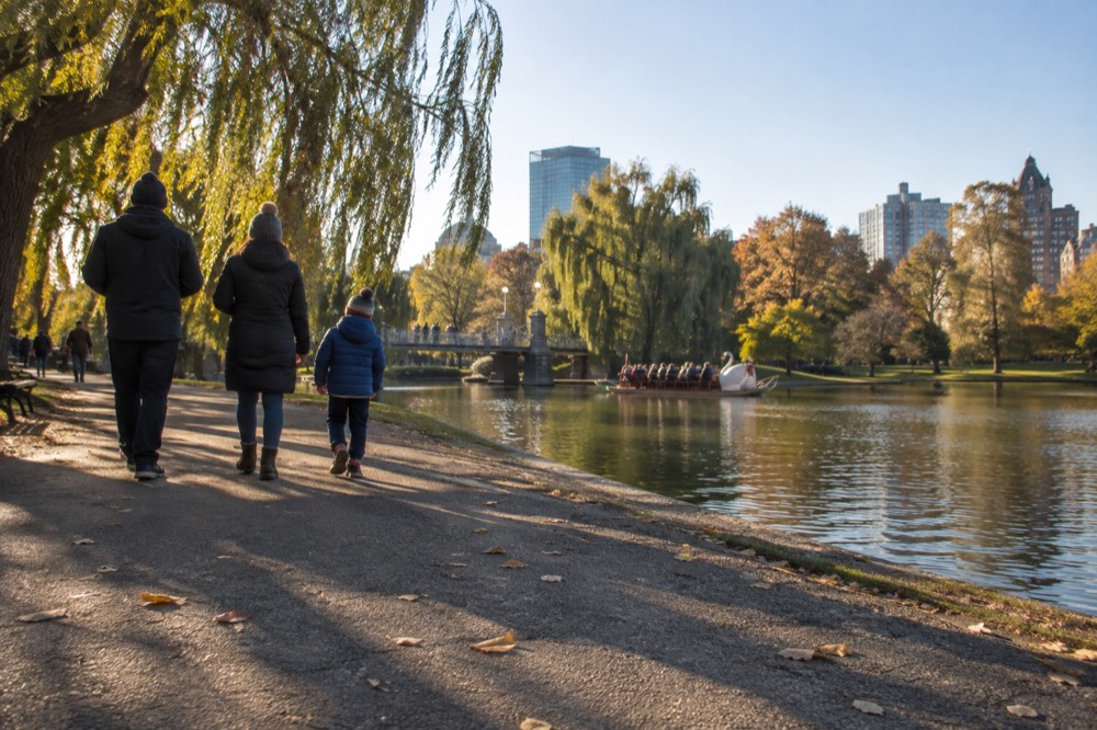 A family walking beside the Swan Boat lagoon in the Boston Public Garden