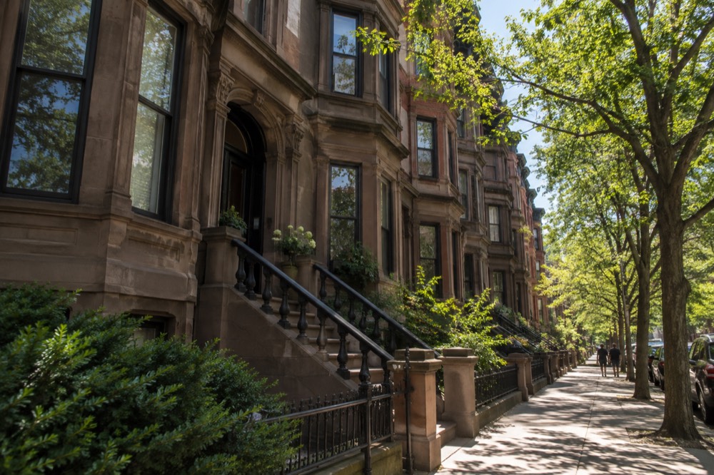 A row of Victorian brownstone townhouses on a Back Bay street with leafy trees