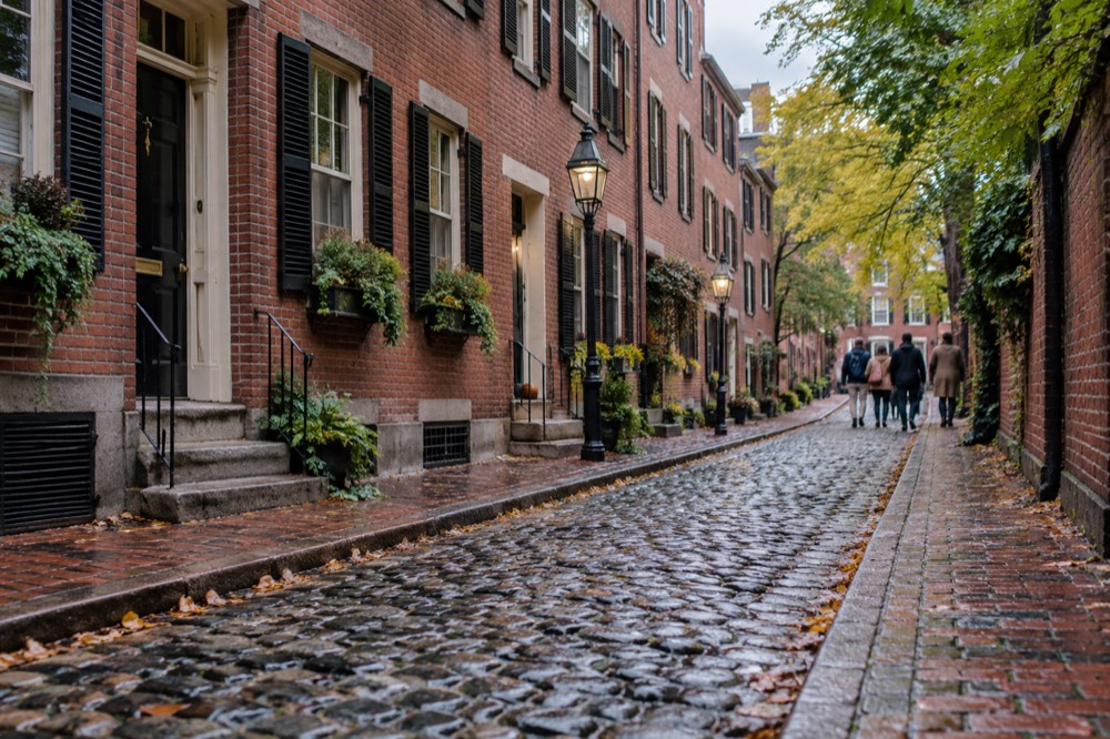 Visitors walking a brick lane in Beacon Hill past row houses with black shutters