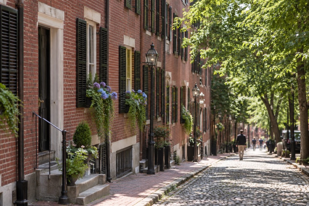 A tree-lined Beacon Hill street with brick rowhouses and flowering window boxes